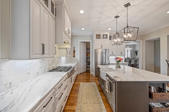 kitchen with an island with sink, backsplash, white cabinetry, hardwood / wood-style flooring, and crown molding