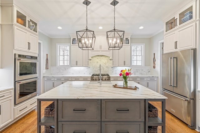 kitchen featuring white cabinets, backsplash, appliances with stainless steel finishes, light stone countertops, and a kitchen island with sink