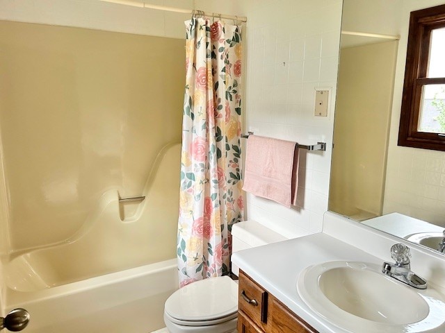 full bathroom with tile walls, shower / tub combo with curtain, toilet, and vanity