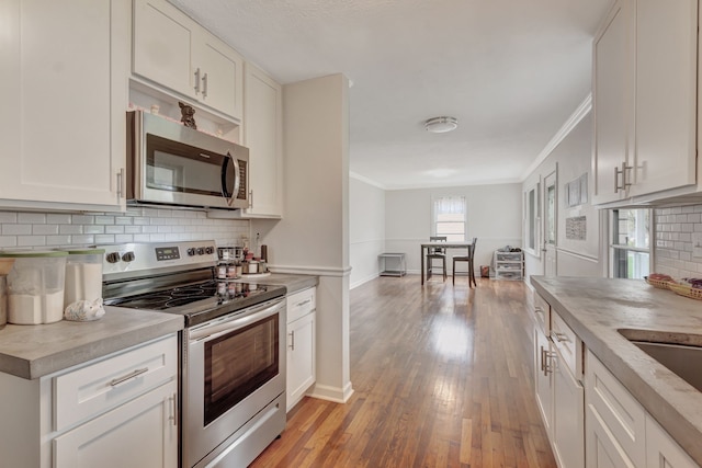 kitchen with appliances with stainless steel finishes, crown molding, white cabinetry, and light hardwood / wood-style floors