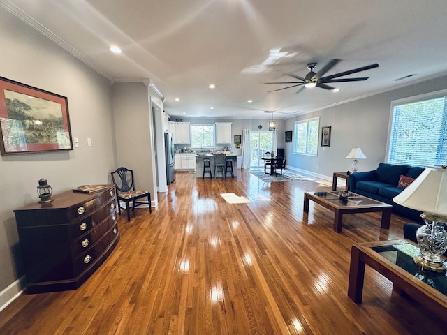 living room with ceiling fan, ornamental molding, and light wood-type flooring