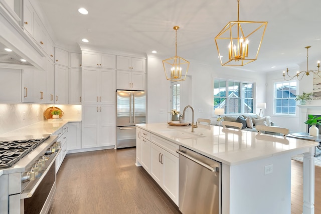 kitchen with high end appliances, pendant lighting, wood-type flooring, premium range hood, and a kitchen island with sink