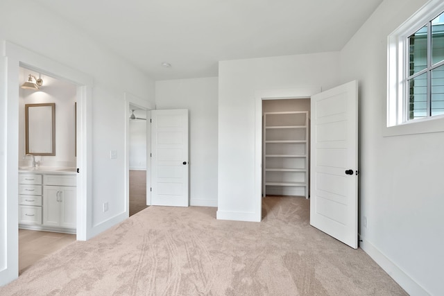 unfurnished bedroom with light colored carpet, a walk in closet, and ensuite bathroom