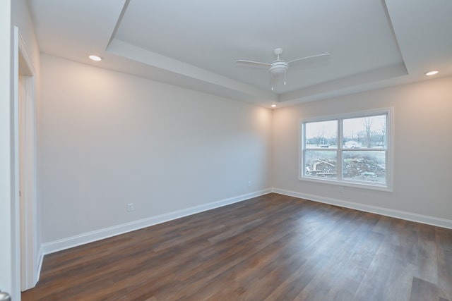 unfurnished room with a raised ceiling, ceiling fan, and dark hardwood / wood-style flooring