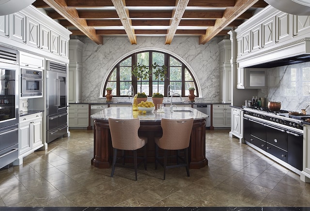 kitchen featuring beam ceiling, dark stone counters, custom exhaust hood, and an island with sink