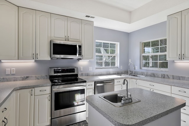 kitchen with stainless steel appliances, sink, a kitchen island, and white cabinetry