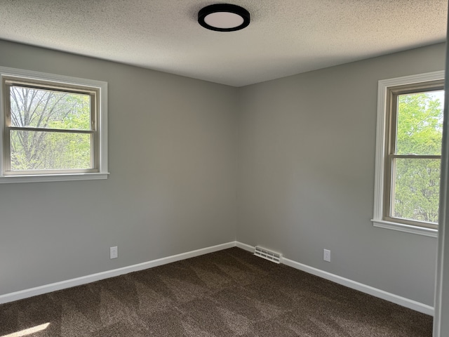 unfurnished room with a textured ceiling, plenty of natural light, and dark colored carpet