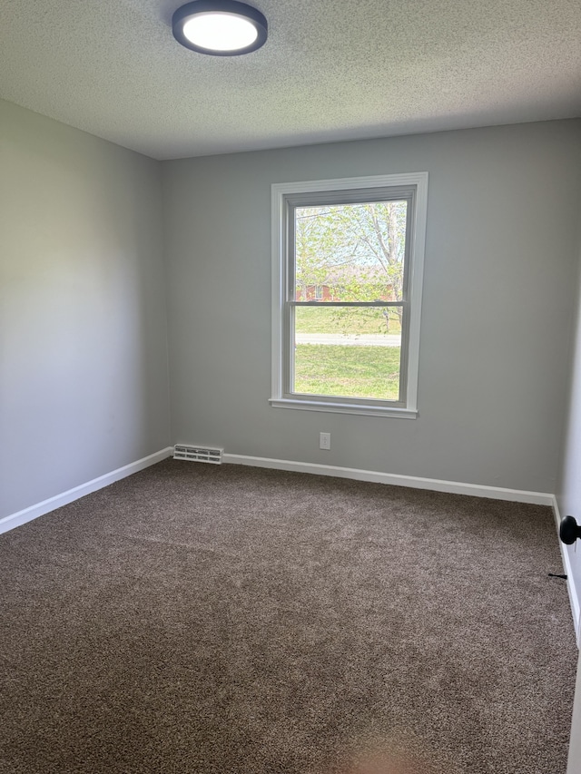 empty room with a textured ceiling and dark colored carpet