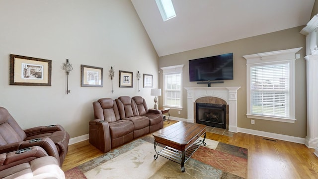 living room featuring a fireplace, high vaulted ceiling, a skylight, and hardwood / wood-style floors