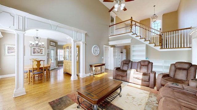 living room with ceiling fan with notable chandelier, light wood-type flooring, a high ceiling, and ornate columns