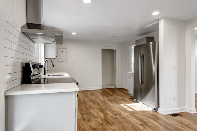 kitchen featuring backsplash, high end fridge, wall chimney range hood, and light wood-type flooring