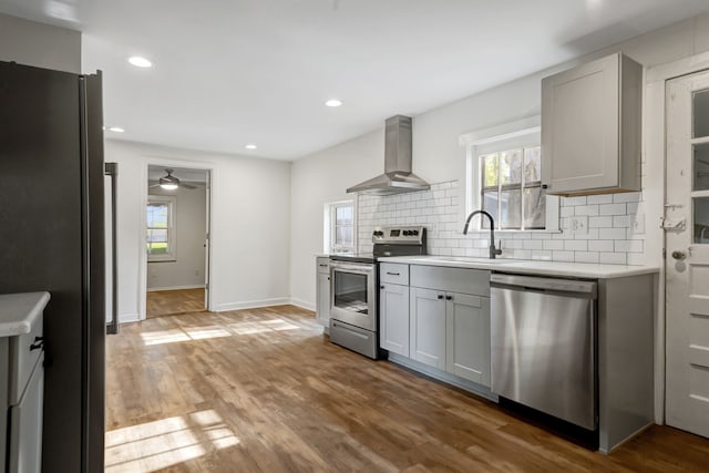 kitchen featuring wall chimney exhaust hood, gray cabinetry, stainless steel appliances, sink, and hardwood / wood-style flooring