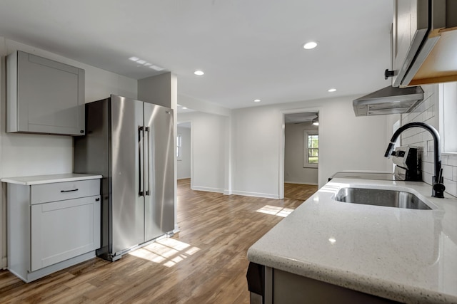 kitchen with light hardwood / wood-style flooring, high end refrigerator, sink, light stone counters, and tasteful backsplash