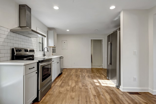 kitchen featuring wall chimney exhaust hood, tasteful backsplash, appliances with stainless steel finishes, and light hardwood / wood-style flooring