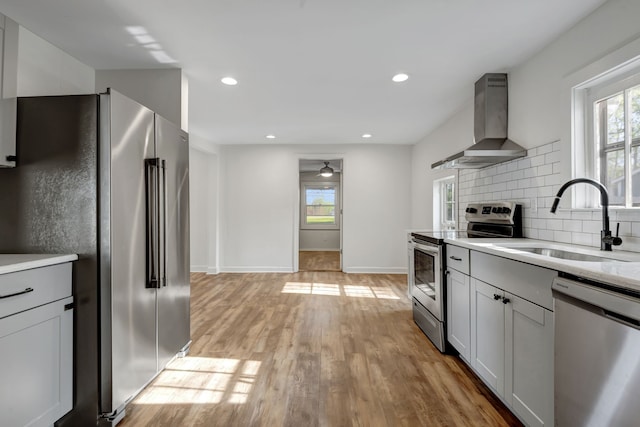 kitchen with appliances with stainless steel finishes, light hardwood / wood-style flooring, tasteful backsplash, wall chimney exhaust hood, and sink