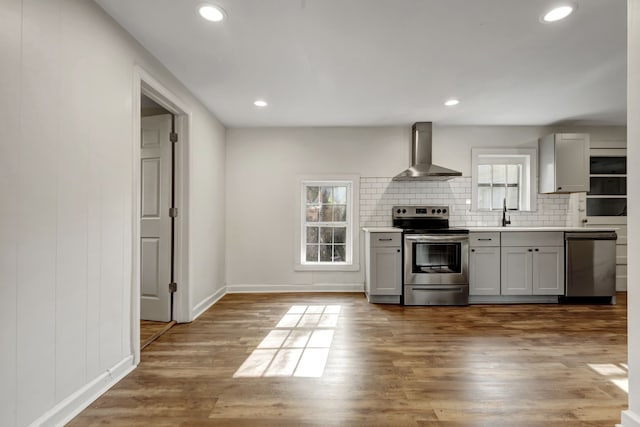 kitchen featuring wall chimney exhaust hood, a healthy amount of sunlight, light hardwood / wood-style flooring, and stainless steel appliances