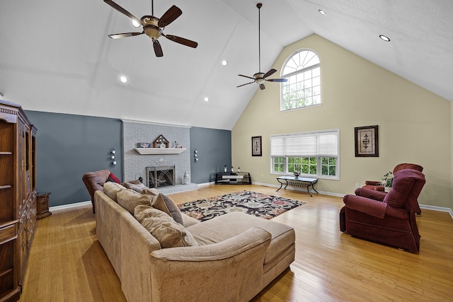 living room with high vaulted ceiling, a brick fireplace, ceiling fan, and light wood-type flooring