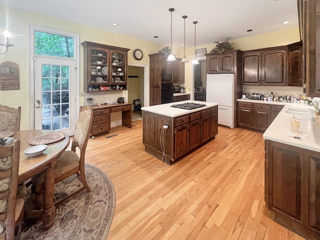 kitchen with backsplash, light hardwood / wood-style flooring, a kitchen island, black oven, and white refrigerator