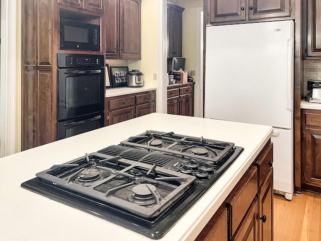 kitchen featuring backsplash, light hardwood / wood-style flooring, dark brown cabinets, and black appliances