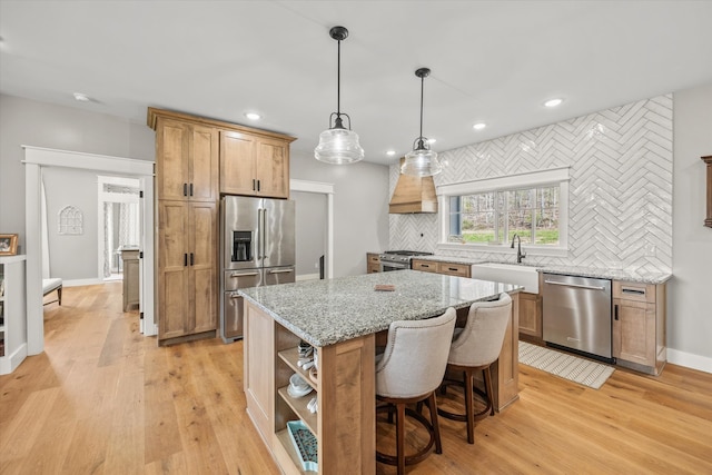 kitchen with high end appliances, light wood-type flooring, a center island, decorative light fixtures, and sink