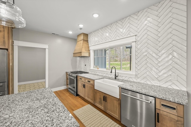 kitchen featuring light wood-type flooring, sink, custom exhaust hood, stainless steel appliances, and light stone countertops