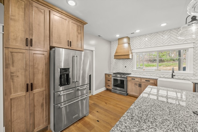 kitchen featuring sink, custom exhaust hood, light hardwood / wood-style flooring, decorative backsplash, and high quality appliances