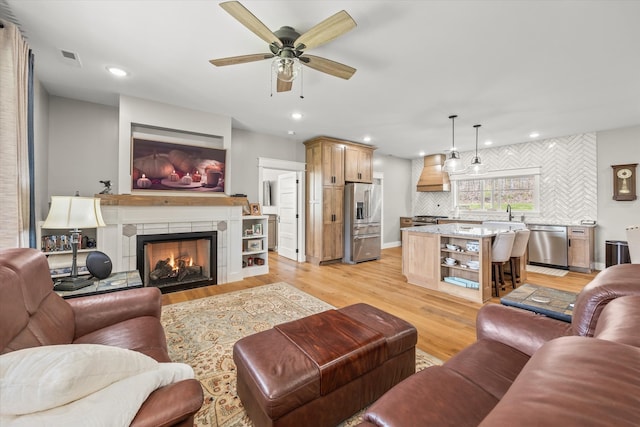 living room with ceiling fan, a fireplace, and light hardwood / wood-style floors