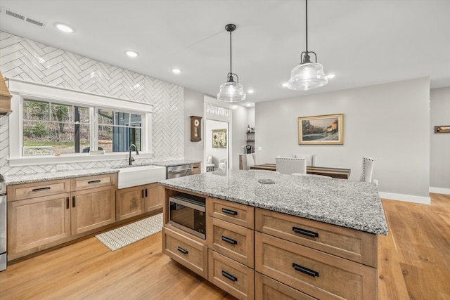 kitchen with decorative light fixtures, stainless steel appliances, sink, and light hardwood / wood-style flooring