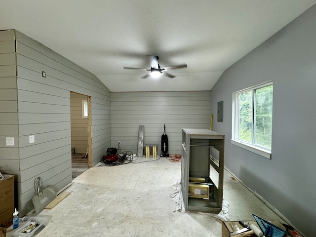 misc room featuring a textured ceiling, lofted ceiling, ceiling fan, wooden walls, and electric panel