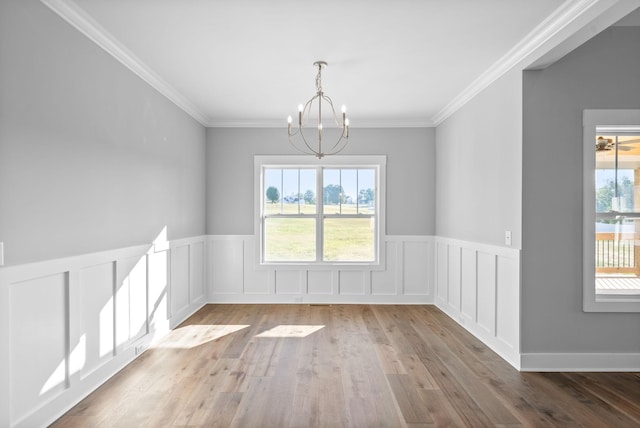 unfurnished dining area with a wealth of natural light, an inviting chandelier, wood finished floors, and ornamental molding