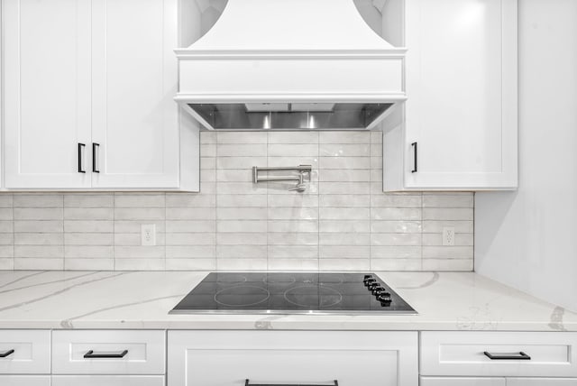 kitchen featuring light stone counters, black electric cooktop, white cabinets, and custom range hood