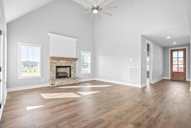 unfurnished living room with visible vents, a stone fireplace, baseboards, and wood finished floors