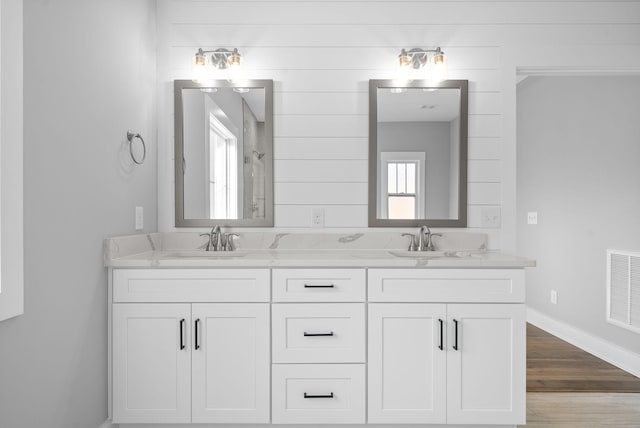 bathroom with a sink, visible vents, wood finished floors, and double vanity