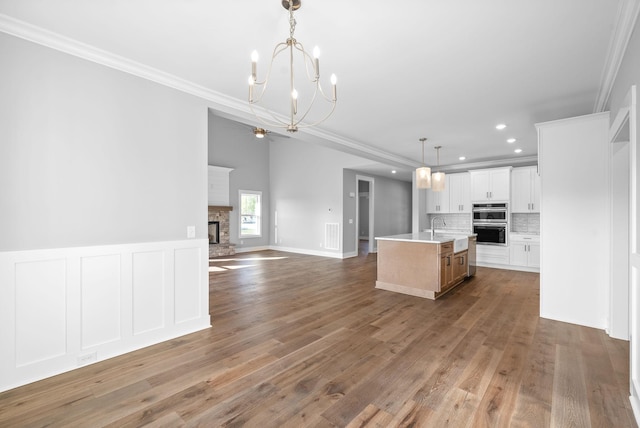 kitchen with backsplash, open floor plan, a stone fireplace, crown molding, and light countertops