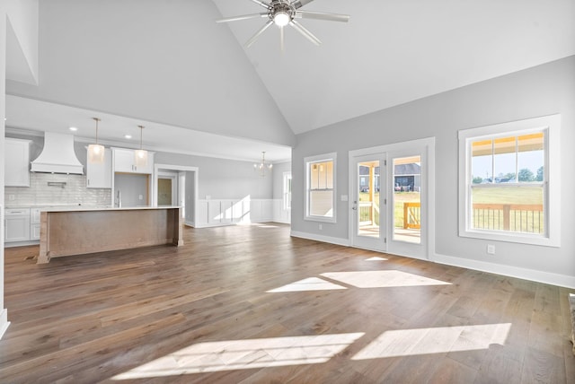 unfurnished living room featuring ceiling fan with notable chandelier, wood finished floors, baseboards, and high vaulted ceiling