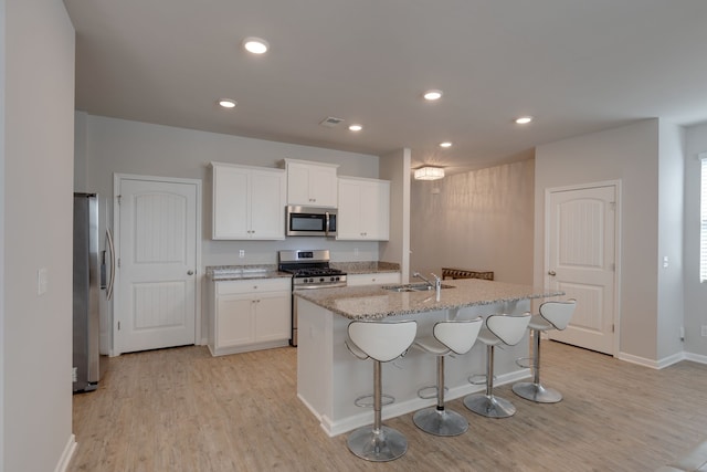 kitchen featuring white cabinets, an island with sink, sink, light hardwood / wood-style flooring, and appliances with stainless steel finishes