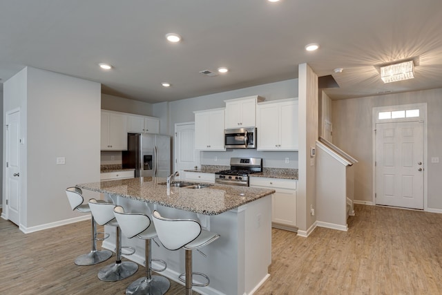 kitchen featuring light stone counters, white cabinetry, light hardwood / wood-style flooring, a center island with sink, and appliances with stainless steel finishes