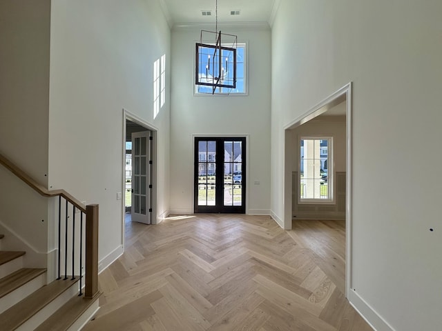 foyer entrance with a chandelier, light parquet floors, a high ceiling, crown molding, and french doors