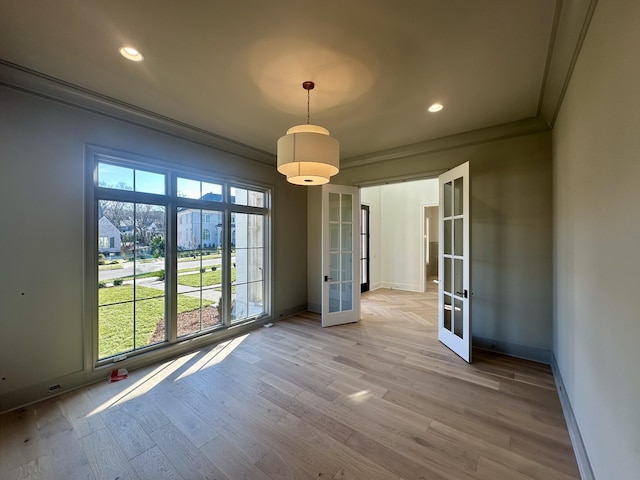 unfurnished dining area featuring crown molding, light wood-type flooring, and french doors