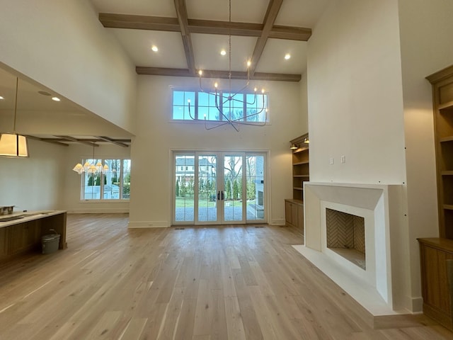 unfurnished living room featuring beam ceiling, coffered ceiling, a notable chandelier, french doors, and light wood-type flooring