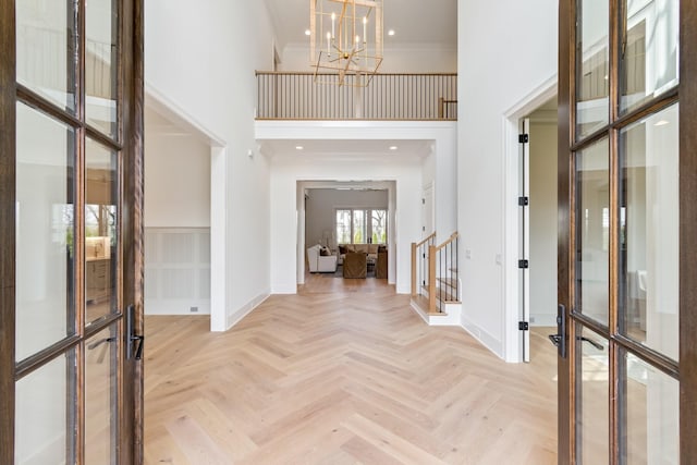 entryway featuring baseboards, an inviting chandelier, ornamental molding, french doors, and a towering ceiling