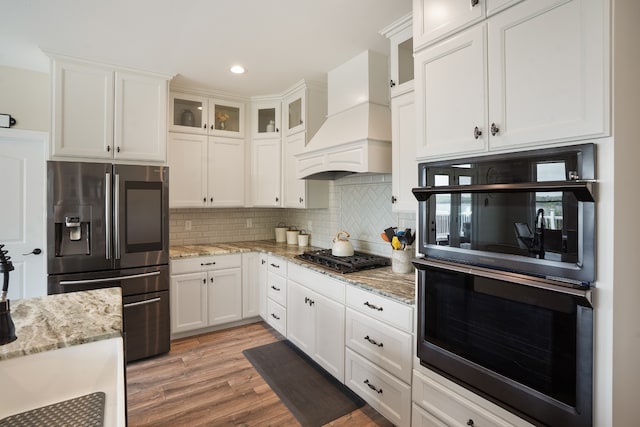 kitchen with backsplash, premium range hood, black appliances, and white cabinetry