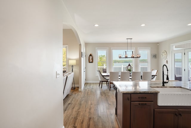 kitchen with light wood-type flooring, decorative light fixtures, light stone counters, sink, and an inviting chandelier