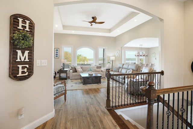 hallway with wood-type flooring, a healthy amount of sunlight, a tray ceiling, and a notable chandelier