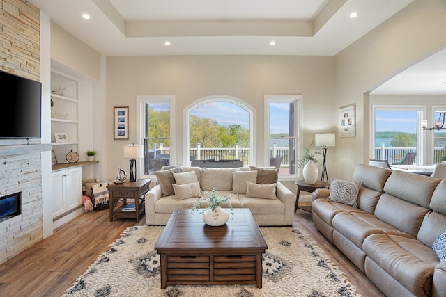 living room with light hardwood / wood-style flooring, a wealth of natural light, built in features, and a stone fireplace