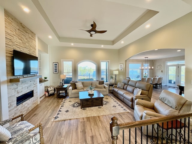 living room with a wealth of natural light, a stone fireplace, light hardwood / wood-style flooring, and a tray ceiling