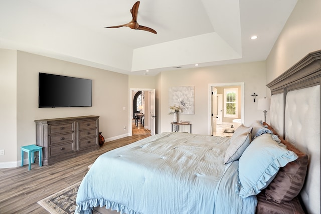 bedroom with hardwood / wood-style floors, connected bathroom, ceiling fan, and a raised ceiling