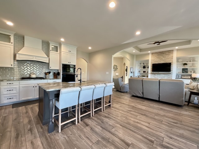 kitchen with custom range hood, light stone countertops, light hardwood / wood-style floors, and white cabinets