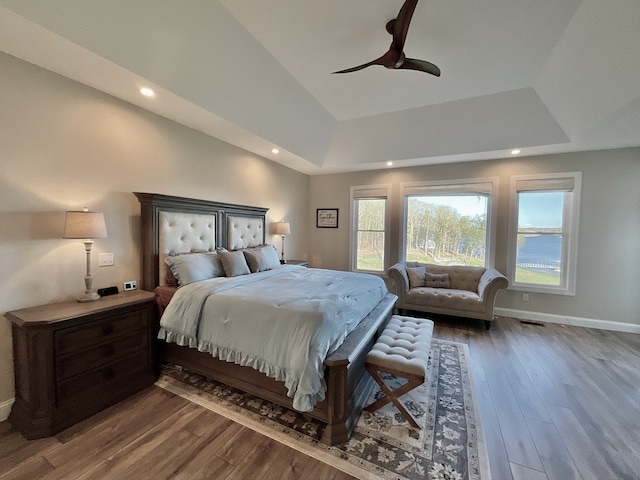 bedroom featuring ceiling fan, a raised ceiling, dark hardwood / wood-style flooring, and multiple windows