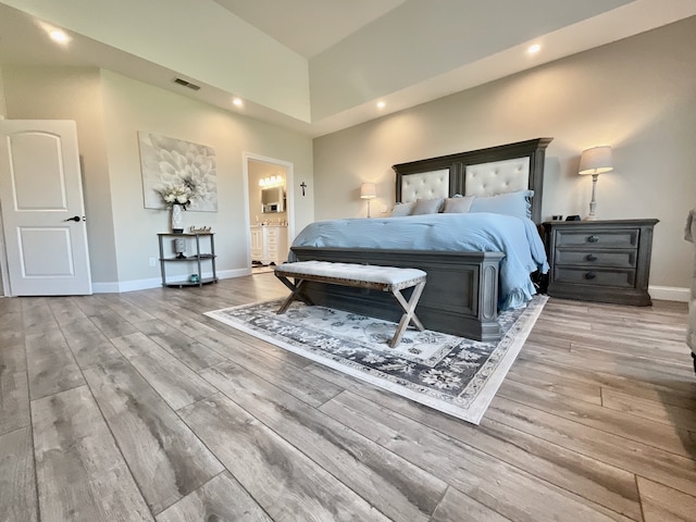 bedroom with light hardwood / wood-style flooring, ensuite bathroom, and a high ceiling